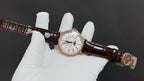 Patek Philippe watch side view with gold bezel, brown leather strap, jeweled accent.