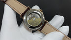Patek Philippe watch case back with engraved details, gold tone, on brown leather strap