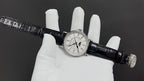 Patek Philippe watch on black leather strap across white gloves, silver clasp visible