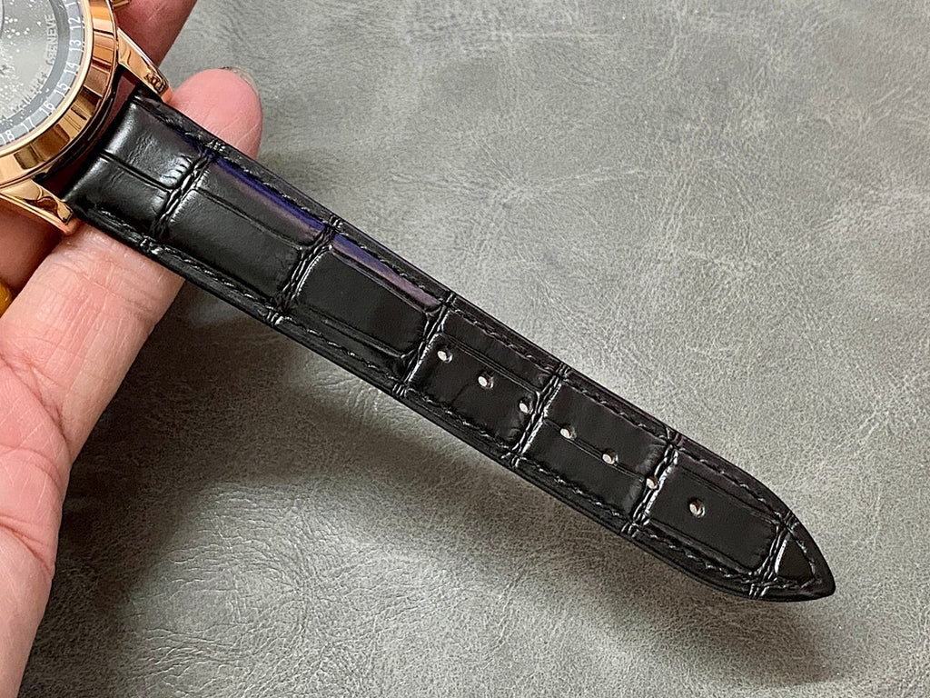 Black leather watch strap with stitched texture and keeper holes, attached to rose-gold lugs