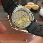 Patek Philippe watch with exposed caseback, black rubber strap, and gold-toned movement