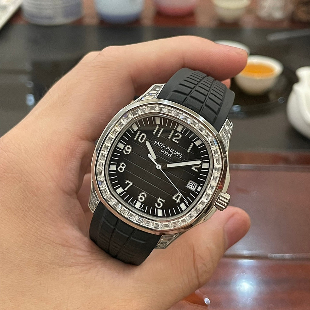 Patek Philippe watch held in hand with black dial, black rubber strap, and silver bezel