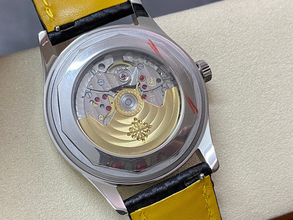 Wristwatch caseback showing gold-toned movement with colored accents; black strap with yellow trim.