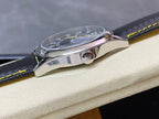 Stainless watch case side with crown and polished bezel; black strap with yellow stitching.
