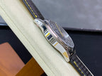 Wristwatch profile with polished stainless case and black strap; yellow contrast stitching visible.