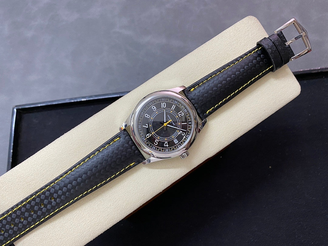 Luxury wristwatch on display pillow with stainless case, dark dial, and black strap with yellow stitching.