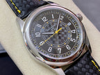 Luxury wristwatch with stainless case, dark patterned dial, yellow hands, and black textured strap.