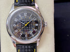 Luxury wristwatch with stainless case, dark dial, date window at 29, and black strap with yellow stitching.