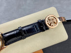 Patek Philippe watch clasp with rose-gold tone emblem on black leather strap