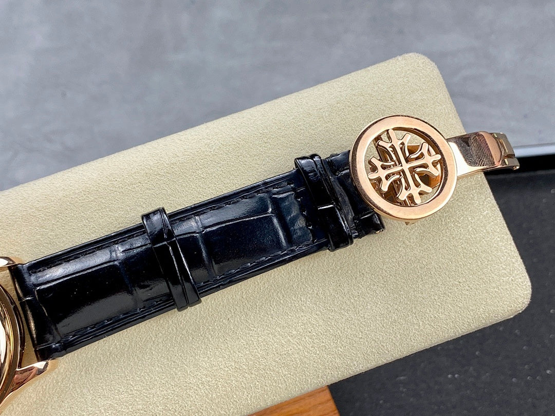 Patek Philippe watch clasp with rose-gold tone emblem on black leather strap