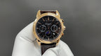 Patek Philippe wristwatch with dark dial, gold bezel, brown leather strap on glove