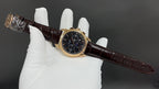 Patek Philippe wristwatch angled view, dark dial, brown leather strap, gold case
