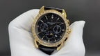 Patek Philippe wristwatch front view with black dial, gold bezel, and leather strap