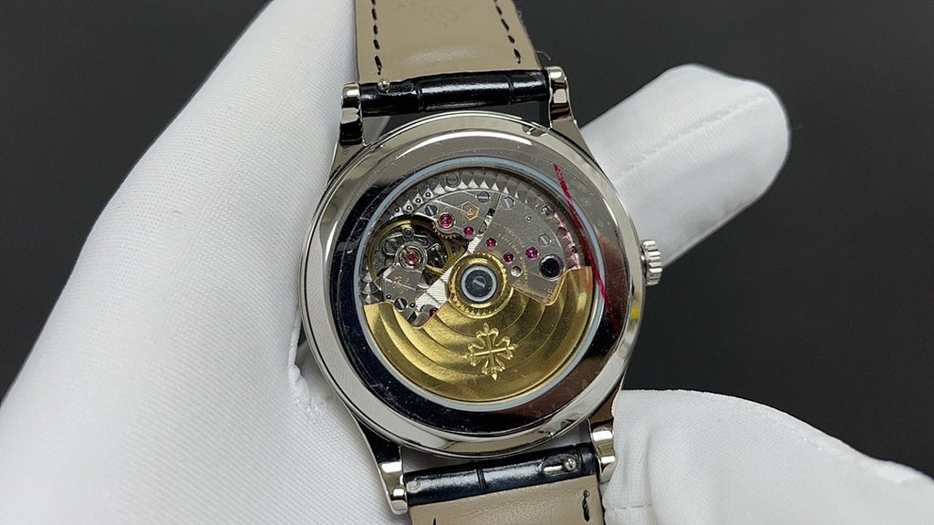 Wristwatch movement view with gold-toned gear and jeweled components under clear cover