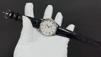 Wristwatch with black leather strap, round silver case, white dial with markers