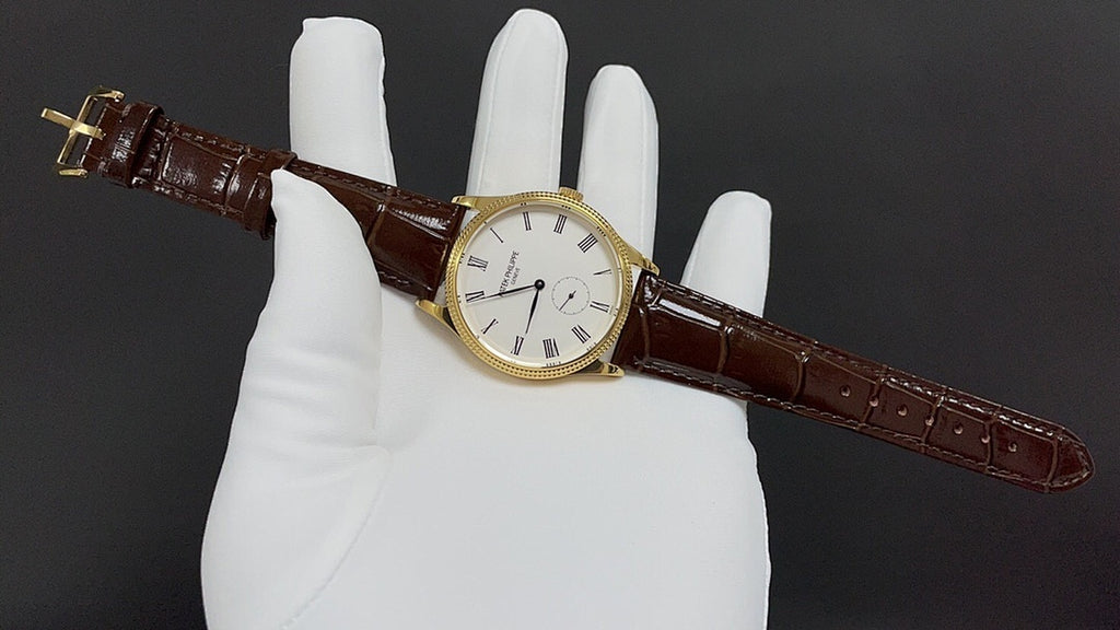 Patek Philippe watch on white gloves, angled view, gold case and brown leather strap