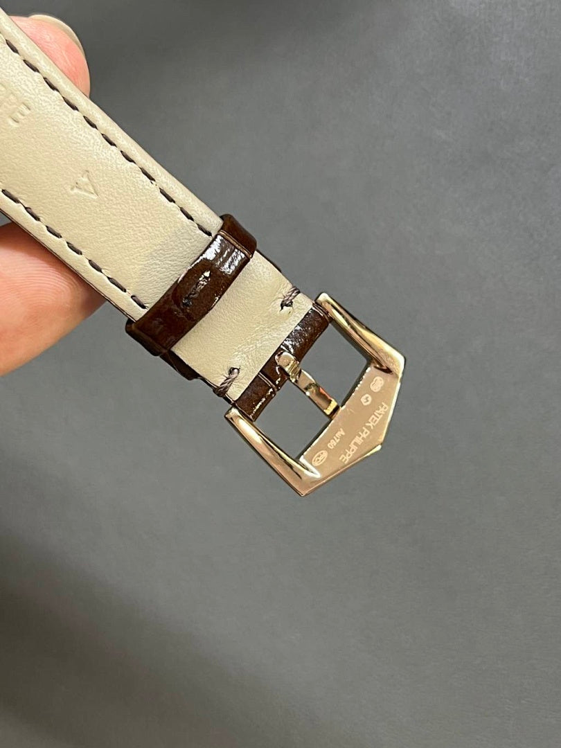 Round wristwatch with brown leather strap and gold-tone buckle; stitched detail