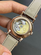 Round wristwatch open caseback with visible components; brown leather strap
