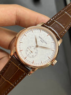 Round wristwatch dial close-up with subdials on white face; brown leather strap