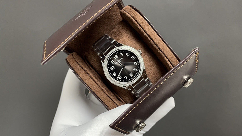 Patek Philippe watch with black dial in brown leather display box, metal bracelet.