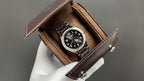 Patek Philippe watch with black dial in brown leather display box, metal bracelet.