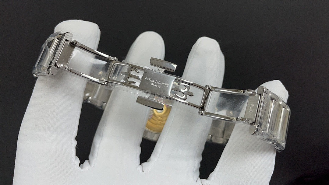 Steel watch bracelet clasp and case back, held in white-gloved hands