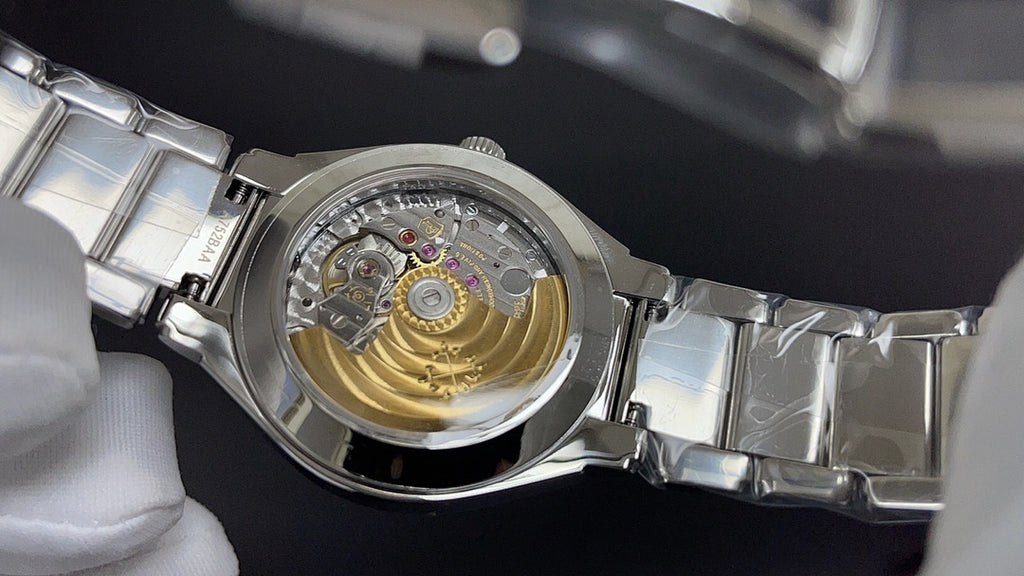 Stainless steel watch case back with visible mechanical movement, held by glove