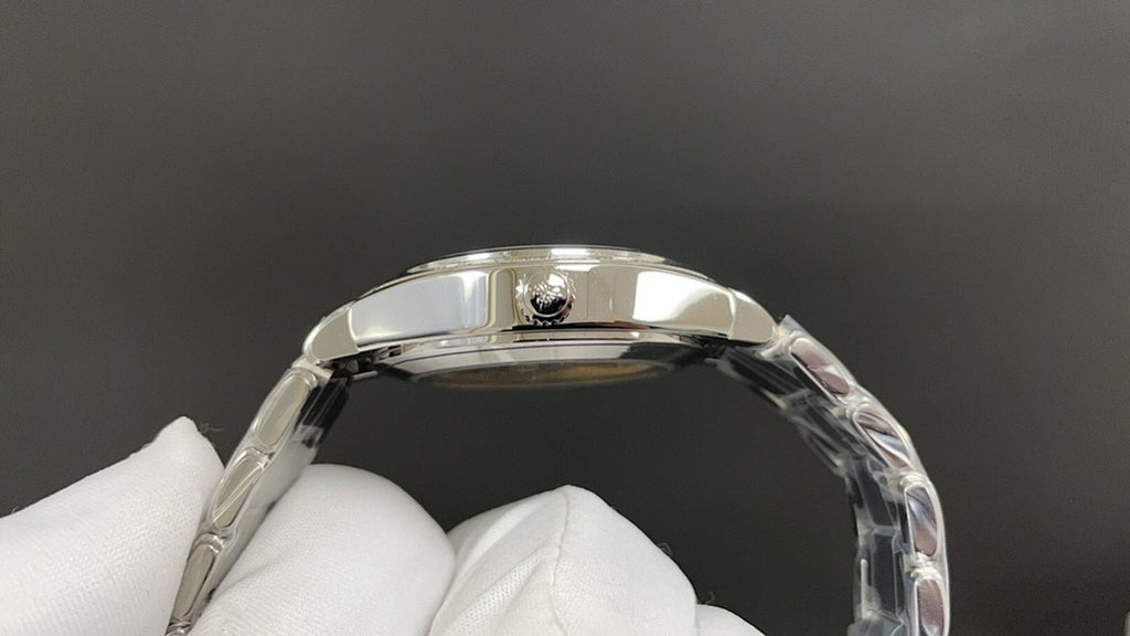 Polished metal watch case top view with crown detail, held in white gloves