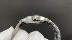 Polished metal watch case top view with crown detail, held in white gloves