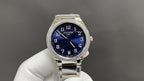 Silver wristwatch with blue dial, diamond bezel, and metal bracelet on glove hand