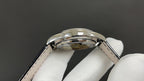 Patek Philippe wristwatch crown and case top, glossy silver-tone finish, black strap