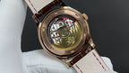 Wristwatch with open case showing mechanical movement, brown leather strap and lugs