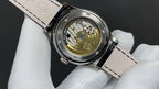 Wristwatch caseback with visible mechanical movement and black leather strap