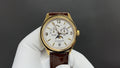 Patek Philippe watch with gold case, white dial, and brown leather strap.