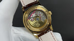 Patek Philippe watch back view with gold case and brown leather strap.