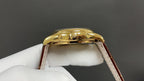 Patek Philippe watch gold case back with brown leather strap on a white glove.