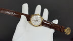 Patek Philippe watch on brown leather strap, gold case, and white dial.