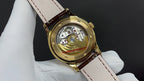 Patek Philippe wristwatch open case view, gold back, visible movement, brown strap