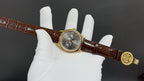 Patek Philippe wristwatch on hand, gold buckle, brown leather strap, round dark dial