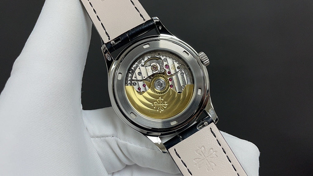 Patek Philippe watch with open caseback showing gold-toned movement, black leather strap