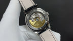 Patek Philippe watch with open caseback showing gold-toned movement, black leather strap