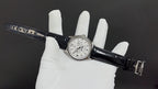 Patek Philippe watch on wrist strap, silver case with white dial and black leather