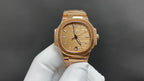 Patek Philippe gold-tone wristwatch with champagne dial and baton markers on white glove.