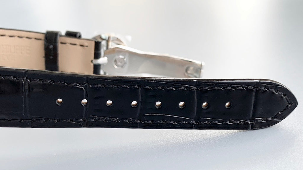 Black leather watch strap with metal buckle and rows of stitch holes