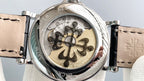 Transparent caseback view with floral-style movement and black leather strap