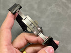 Black watch strap with metal clasp and underside hardware, shown at an angle