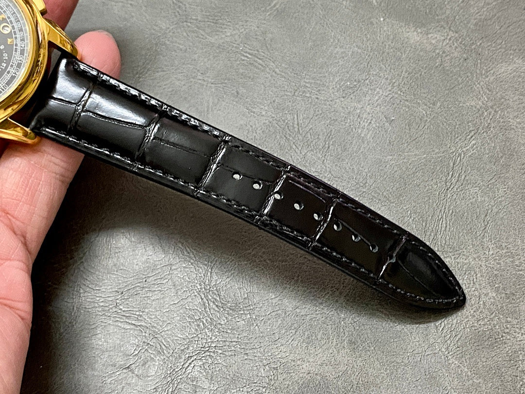 Black leather watch strap with stitching and buckle holes, glossy finish.