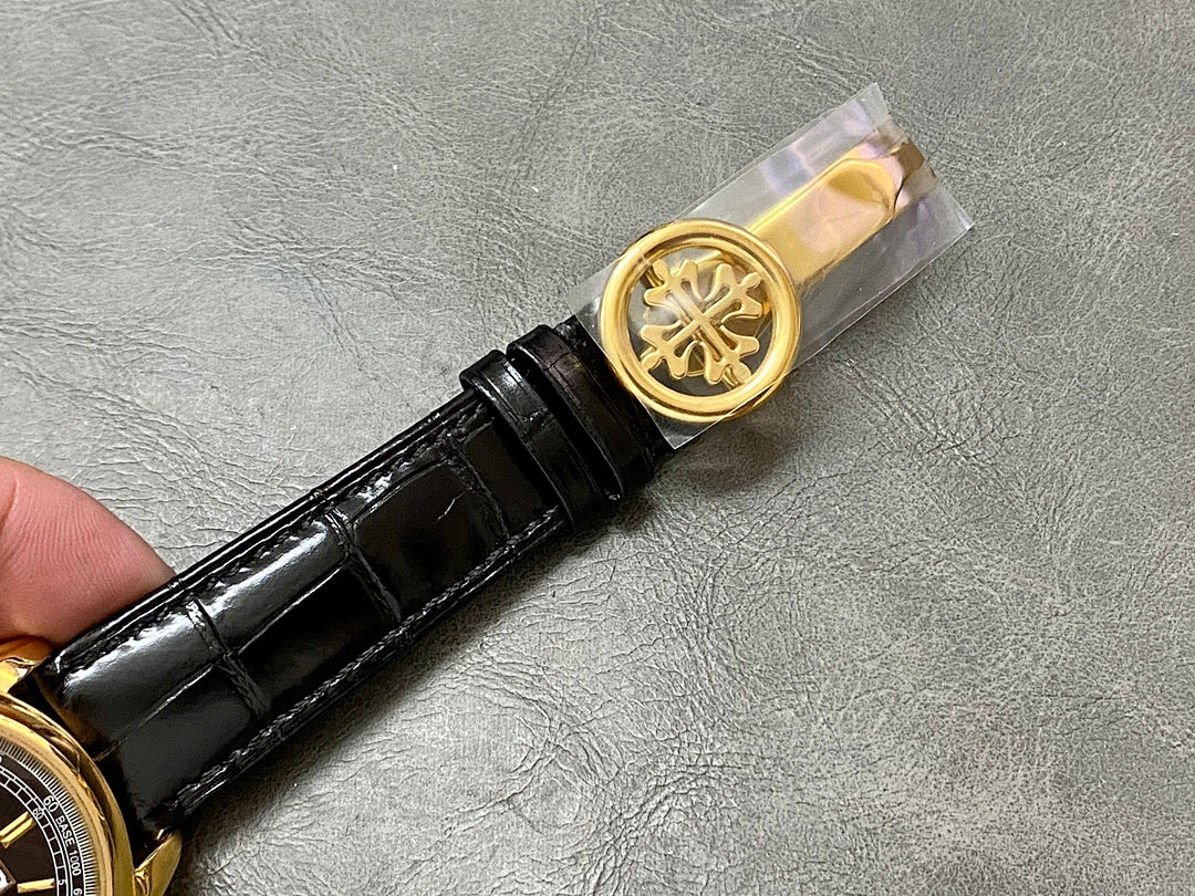 Black leather watch strap with gold buckle and embossed emblem clasp.