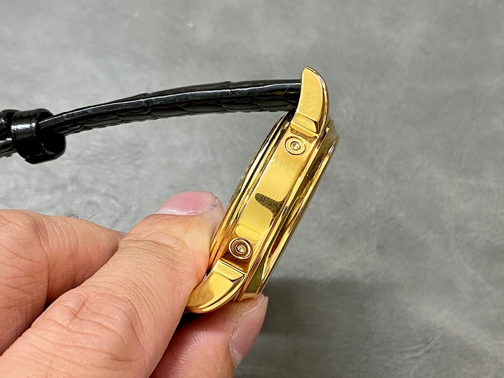 Gold watch side view with pushers and crown; black leather strap attached.