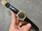 Gold wristwatch on black leather strap with black chronograph dial and subdials.